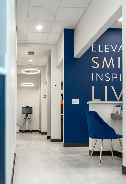 Modern dental office hallway with treatment rooms, seating, and blue accent walls.
